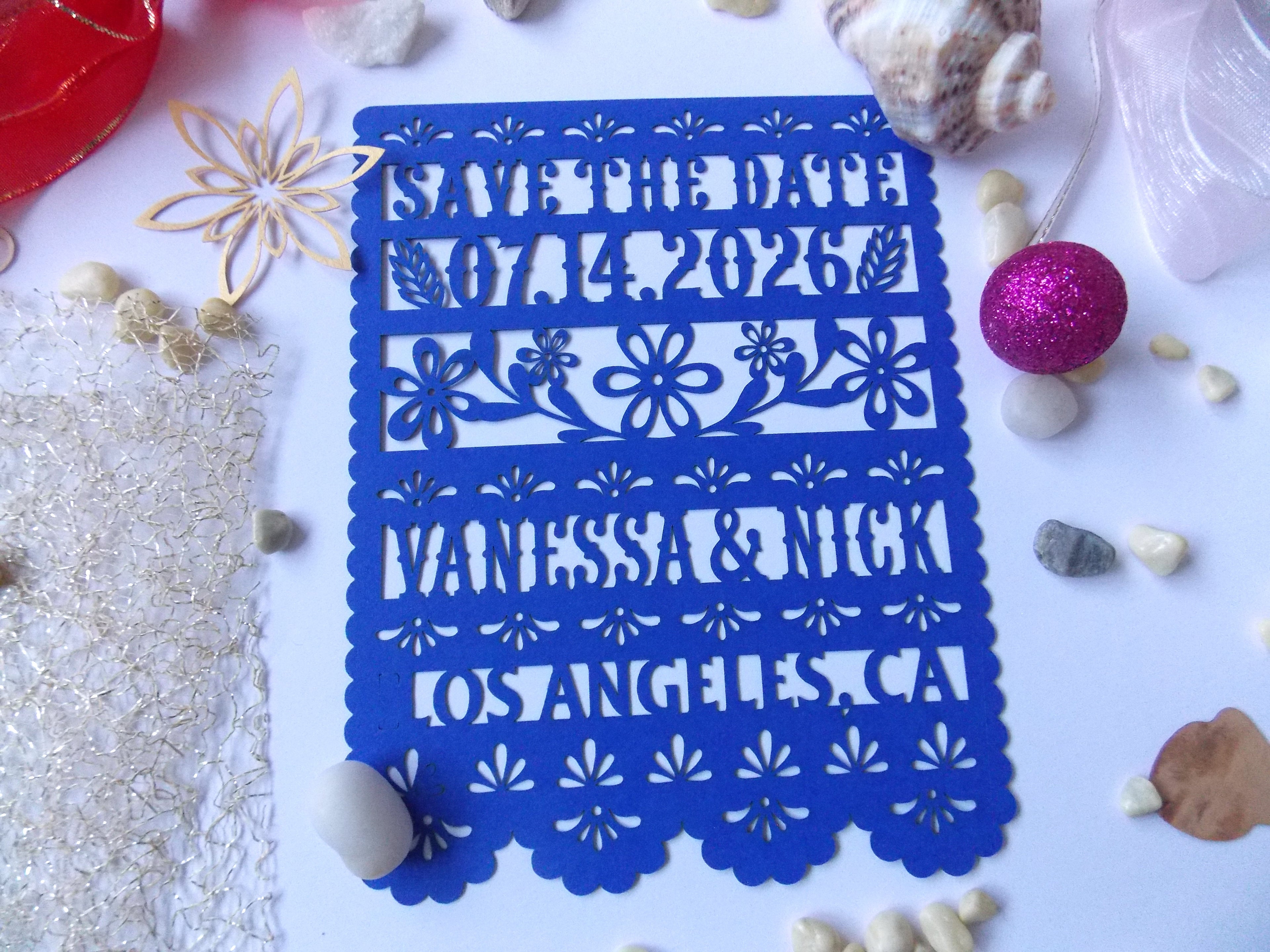 Blue 'Save the Date' card with floral patterns on a white surface with decorative items.