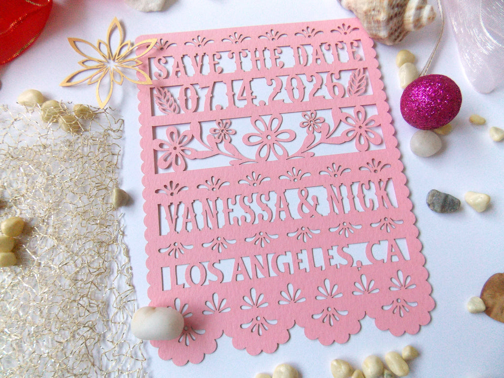 Pink 'Save the Date' card with floral patterns in papel picado style with decorative items.