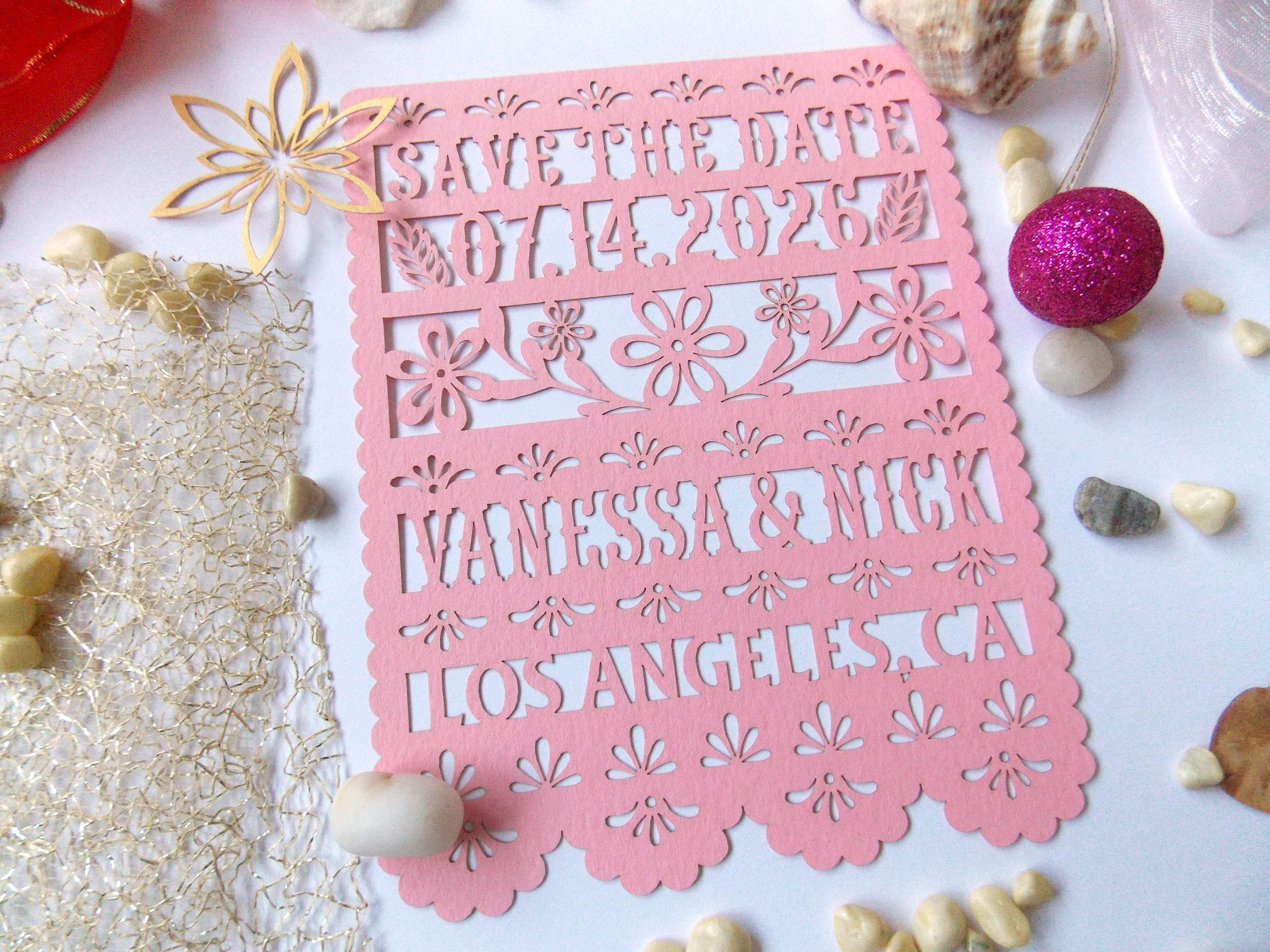 Pink 'Save the Date' card with floral patterns in papel picado style with decorative items.
