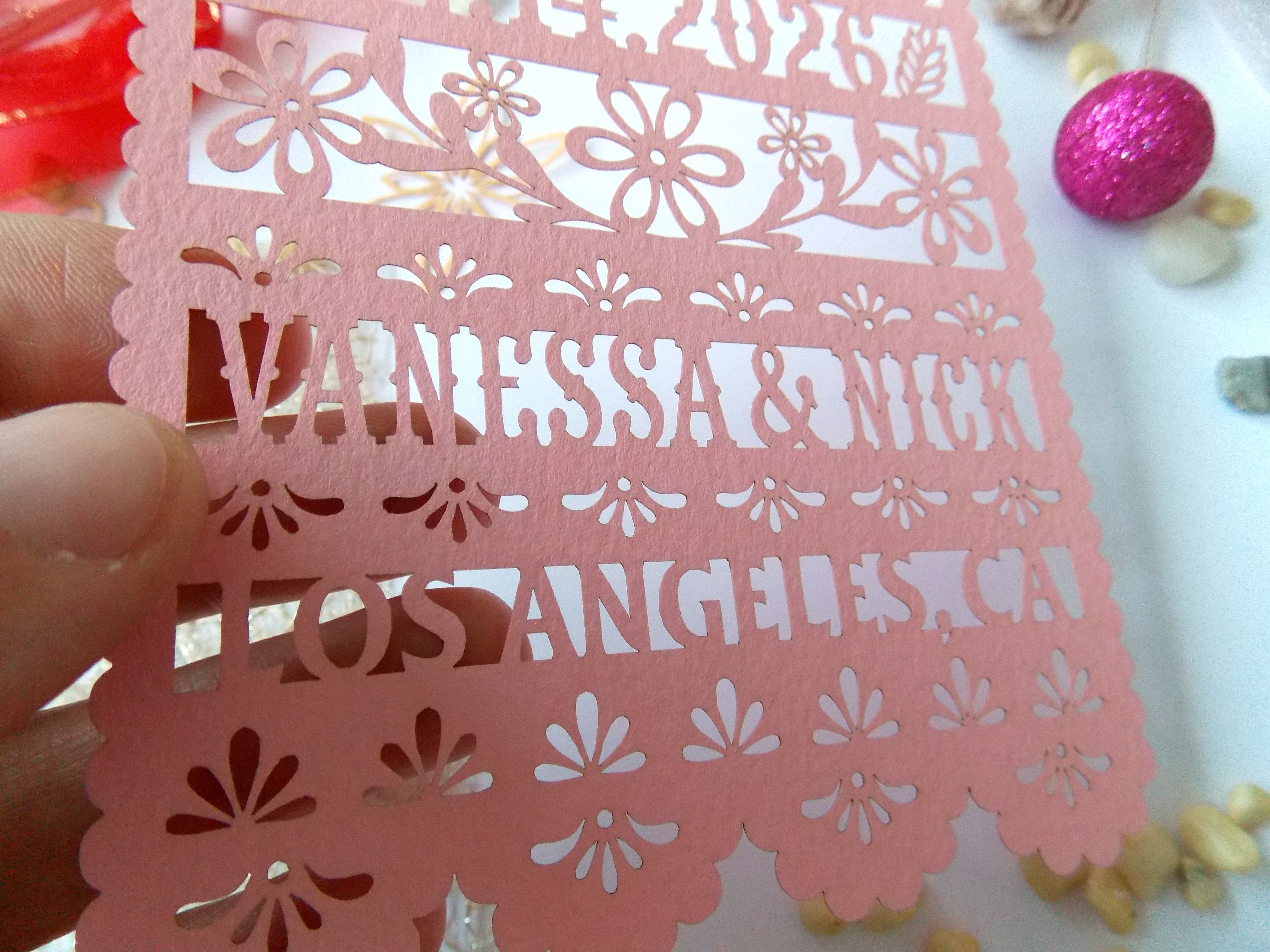 Rose color save the date with cut-out designs and text held by a hand.